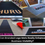 Collage of four branded entrance mats placed in commercial spaces, each displaying company logos. A caption below reads, &ldquo;Can Branded Logo Mats Really Enhance Business Visibility?&rdquo; showing examples of custom logo floor mats used for branding at entrances.